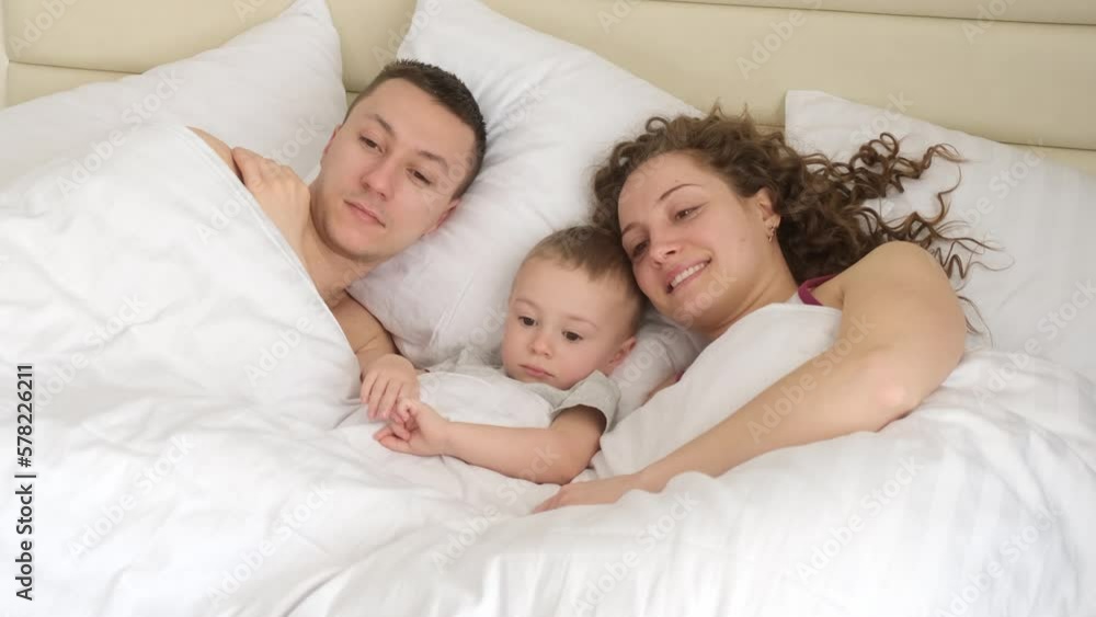 Happy young family with a child lying on the bed at home during vacation. Family relationships and family vacation concept Happy young family with a child lying on the bed at home during vacation. Family relationships and family vacation concept