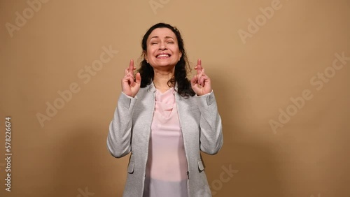 Middle-aged pretty woman crossing fingers, with prayerful hopeful look, makes cherished wishes, hopes her dream comes true, wishing for fortune or good luck, isolated background. People. Emotions photo