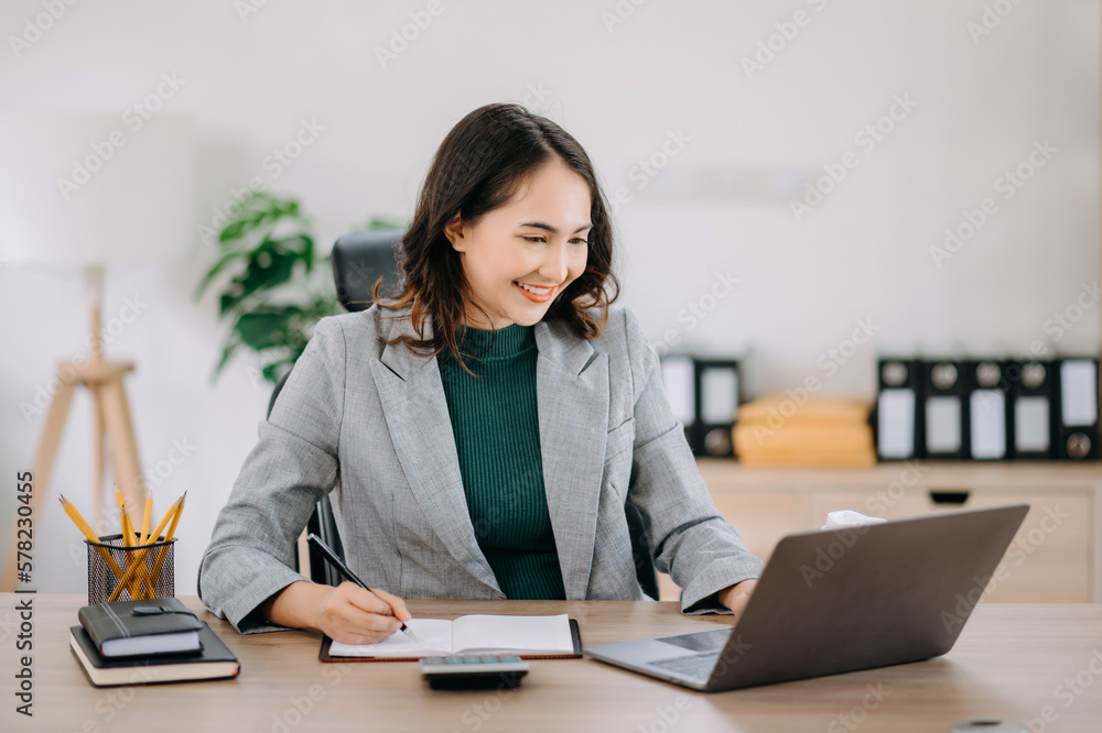 Beautiful Asian woman using laptop and tablet while sitting at her working place. Concentrated at work.. Beautiful Asian woman using laptop and tablet while sitting at her working place. Concentrated at work..