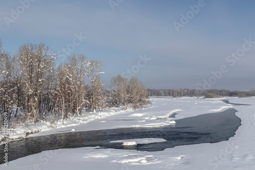 winter river with thaw and forest on the bank