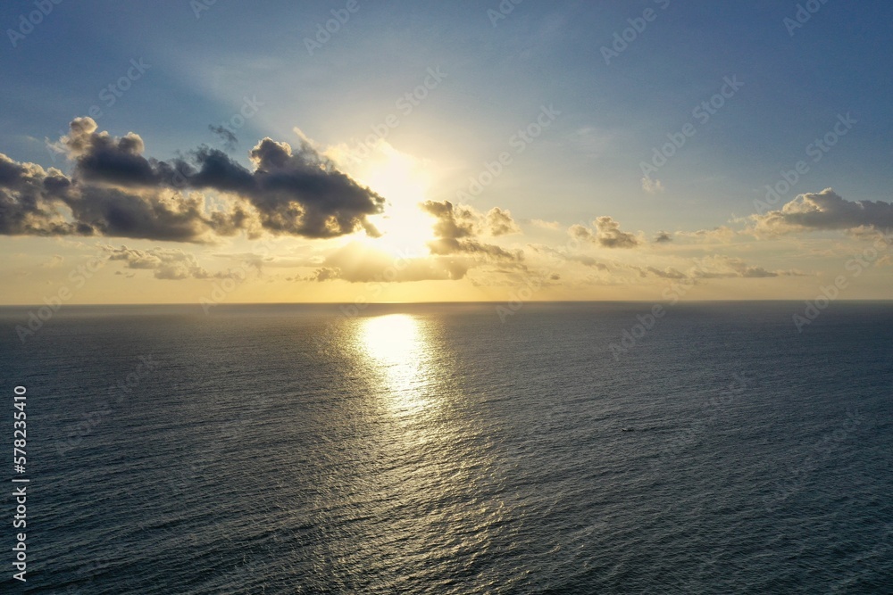 Shot of a golden burning sun in the cloudy sky about to set on the horizon of the sea.