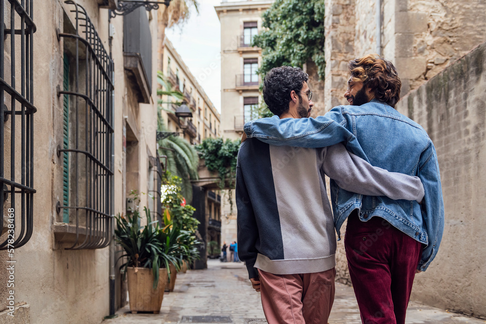 gay male couple walking embraced along a beautiful ancient street decorated with plants, concept of leisure and love between people of the same sex