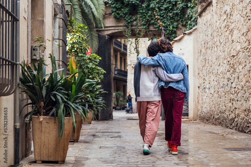 rear view of a gay male couple walking embraced along a beautiful ancient street decorated with plants, concept of leisure and love between people of the same sex