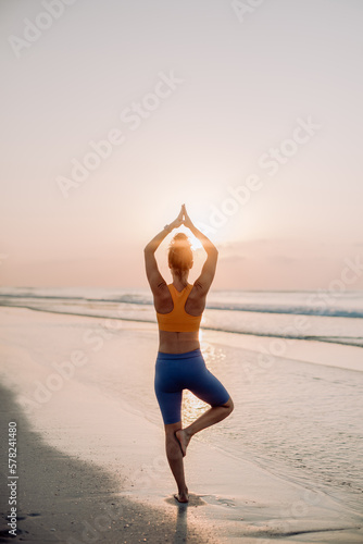 Rear view of young woman taking exercises at beach  morning routine and healthy lifestyle concept.