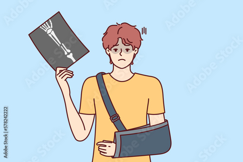 Man injured arm and shows picture of bone with traces of fracture taken by doctor using X-ray machine. Guy injured in car accident has broken arm and needs treatment or rehabilitation 