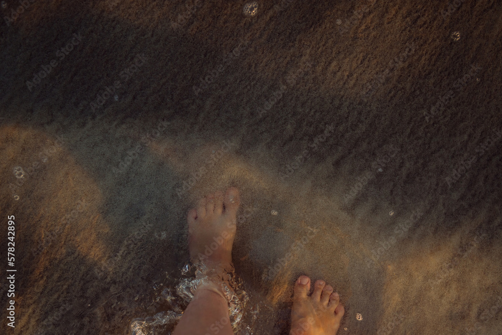 Woman walking on a beach during sunset, close-up of feet.