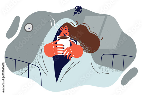 Woman suffering from melancholy sits on bed wrapped in blanket and drinks hot coffee 