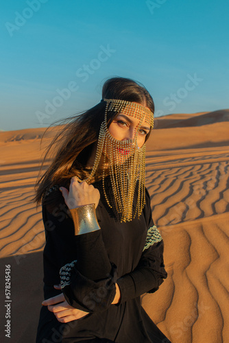 Beautiful woman in brilliant Burqa mask among the Dubai desert at sunset time.Arabian style