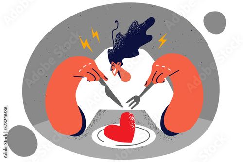 Aggressive woman sits with fork and knife in hands near plate with heart as symbol of dominance