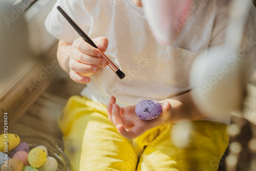 Kids hands paint easter eggs with brush in different colors. Close up view.