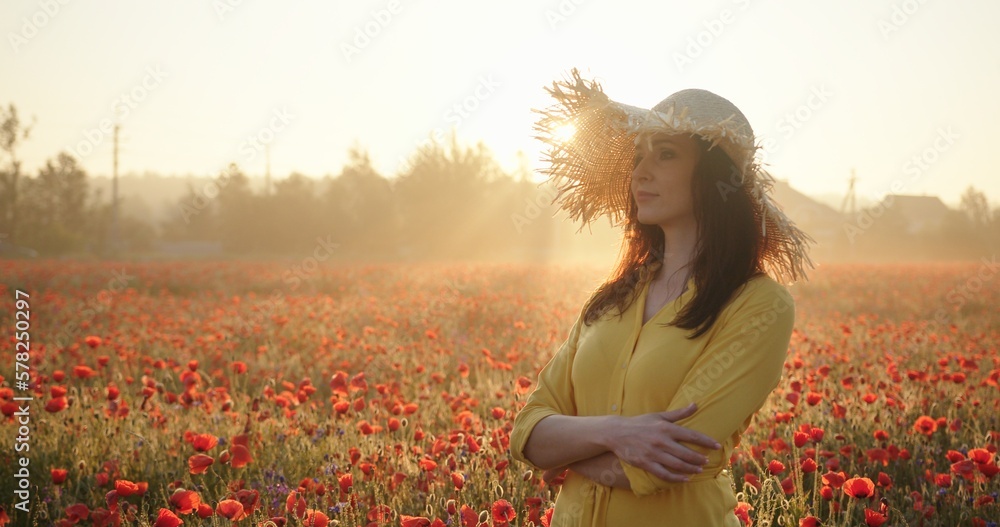 Brunette woman in a yellow dress and straw hat in poppy field at sunrise. Harmony, love, nature concept Brunette woman in a yellow dress and straw hat in poppy field at sunrise. Harmony, love, nature concept