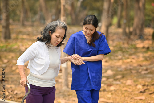 Image of caring female caregiver helping senior woman walking in the park. Assistance and rehabilitation concept © Prathankarnpap