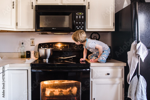 young boy sitting on counter looking at oven timer while cookies bake photo
