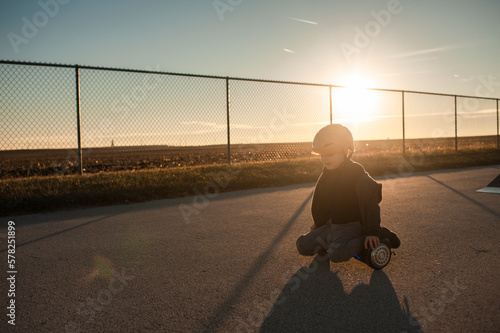 Young boy riding hover board in warm sunlight near fence