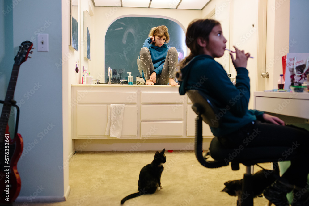Girl sits on bathroom counter brushing hair and sister brushes teeth Girl sits on bathroom counter brushing hair and sister brushes teeth