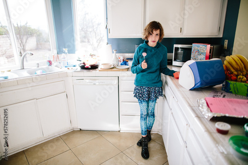 Girl in her kitchen looks toward camera annoyed