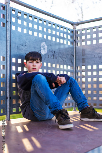 Portrait of young boy sitting looking camera,leaning on metallic fence photo