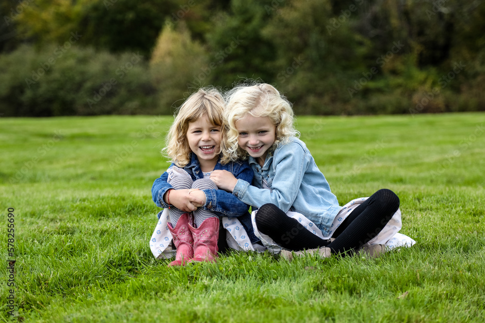 two sisters sitting on grass smiling towards camera linked arms two sisters sitting on grass smiling towards camera linked arms