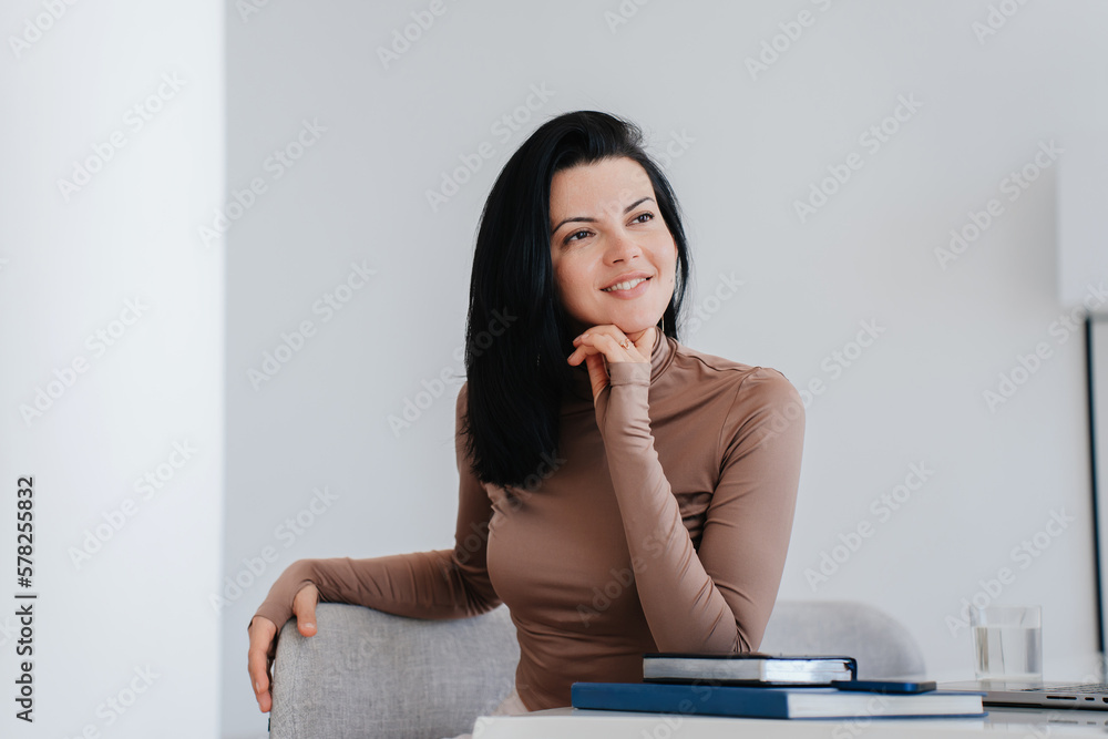 Dreamy brunette hispanic businesswoman sitting at desk with books looks away smiles, planning agenda, dreaming about career. Purposeful writer work home. Beautiful woman relaxing indoors. Successful Dreamy brunette hispanic businesswoman sitting at desk with books looks away smiles, planning agenda, dreaming about career. Purposeful writer work home. Beautiful woman relaxing indoors. Successful