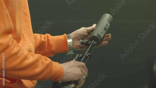 A man screws a silencer on a Kalashnikov assault rifle