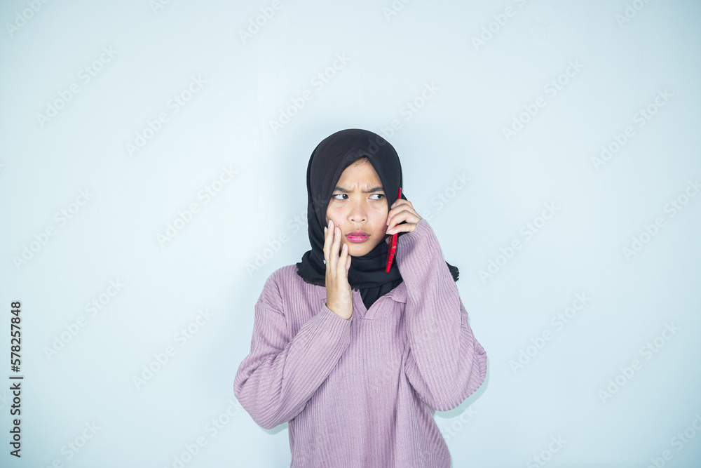 young woman in hijab confused while looking at smartphone screen with hand scratching head young woman in hijab confused while looking at smartphone screen with hand scratching head