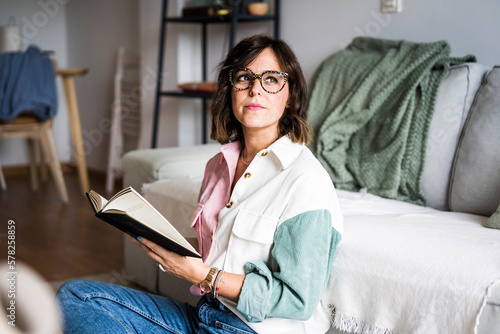 Thoughtful woman sitting with book at home photo