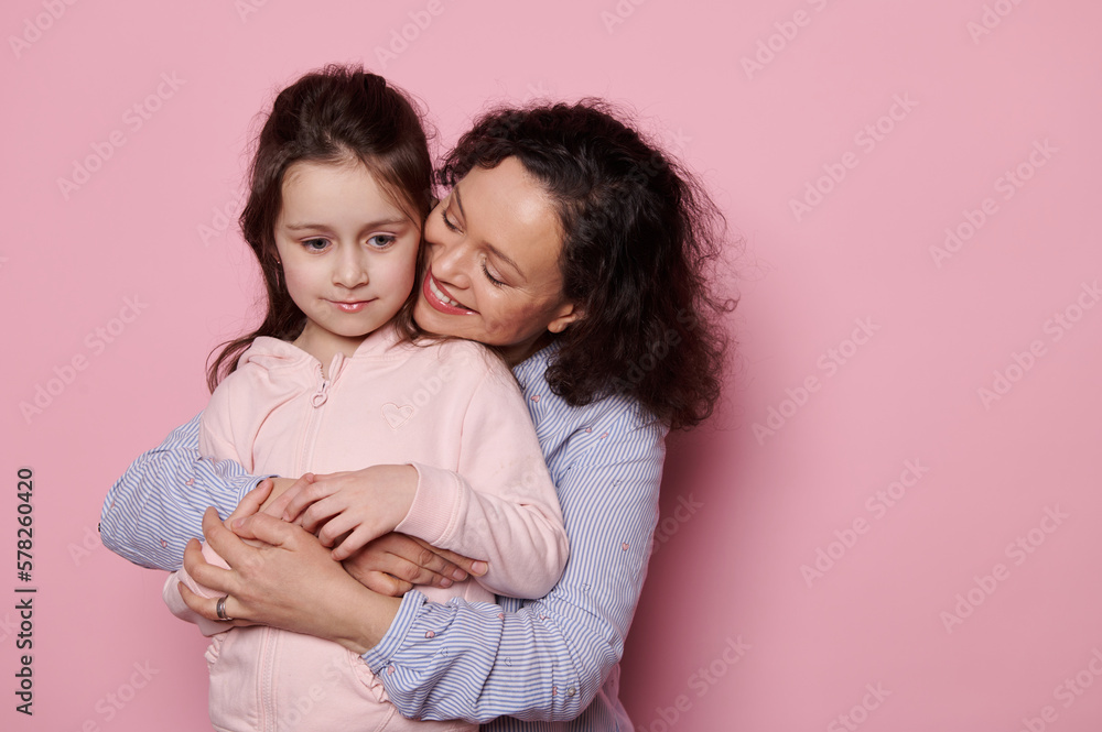 Happy pretty woman hugging her little kid daughter from behind, isolated on pink background studio portrait. Mommy and child have fun together. Mother's Day. Love Family Parenthood Childhood concept Happy pretty woman hugging her little kid daughter from behind, isolated on pink background studio portrait. Mommy and child have fun together. Mother's Day. Love Family Parenthood Childhood concept