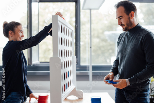 Happy businesswoman with colleague playing connect four dots game in office photo