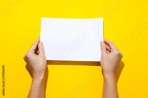 Female hands hold blank paper on yellow background