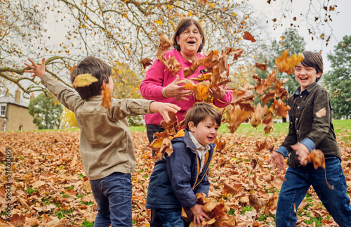 Grandmother playing with grandsons throwing autumn leaves at park photo