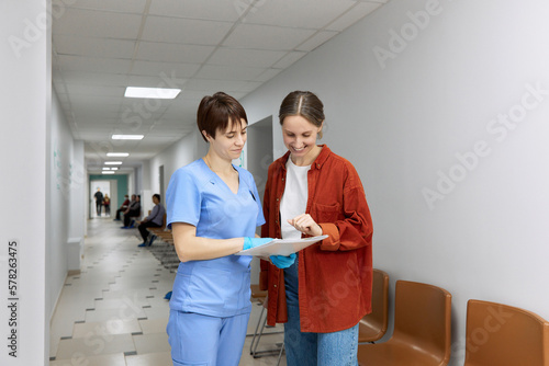 Doctor and patient reviewing test results standing in corridor at hospital photo
