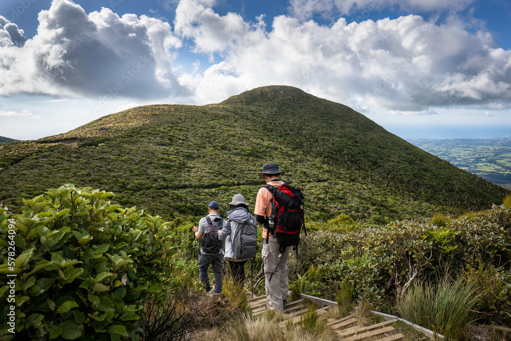 Three people hiking Pouakai circuit with views of the Taranaki coastline, Egmont National Park. New Zealand. Three people hiking Pouakai circuit with views of the Taranaki coastline, Egmont National Park. New Zealand.