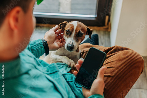 Man holding smart phone and stroking dog at home photo