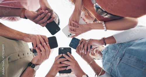 Hands, phone and communication with friends standing in a huddle or circle from below for networking. Social media, mobile and 5g with a man and woman friend group connected to the internet together