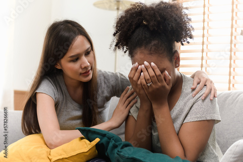 Φωτογραφία Multi ethnic young woman friend consoling her crying African ethnic friend while sitting on sofa