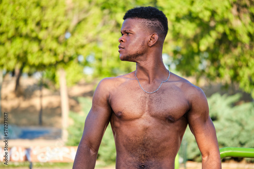 Portrait of a young fit shirtless black man looking at a side in a park outdoors. Fitness and sport lifestyle.