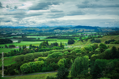 Iconic New Zealand Landscape with green rolling hills and distant mountain range under cloudy sky. Greys Hill Lookout, Gisborne, North Island, New Zealand photo