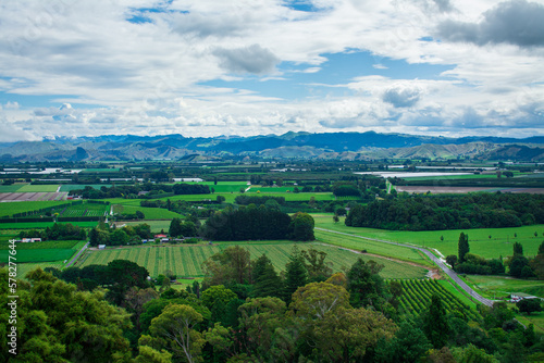 Aerial view over lush green farmland, distand mountain range rising over horizon under cloudy sky. Breathtaking New Zealand Landscape. Greys Hill Lookout, Gisborne, North Island, New Zealand