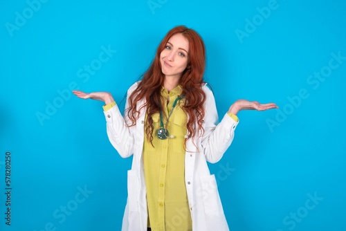 Careless attractive young doctor woman wearing medical uniform over blue background shrugging shoulders  oops.
