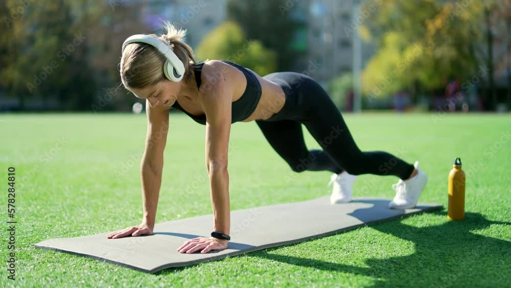 Fit woman with headphones doing gymnastics on a mat in an urban city