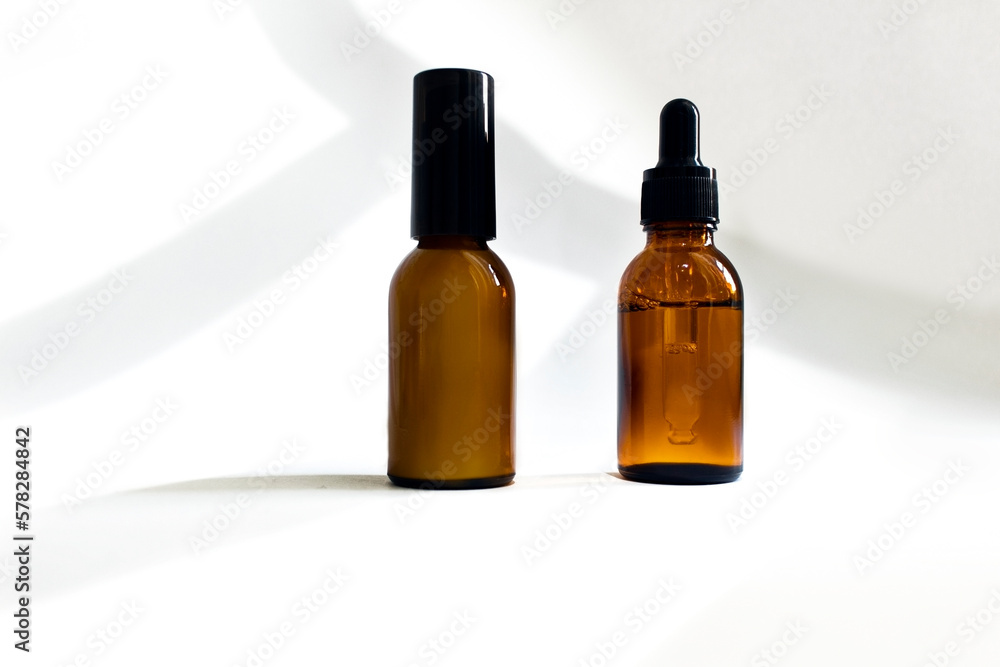 Glass cosmetic bottles with a dropper on a white background with hard shadows. The concept of natural cosmetics, natural essential oil