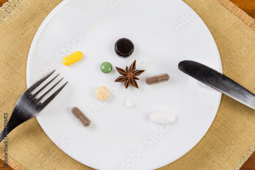 Different pills on white dish with cutlery on the table