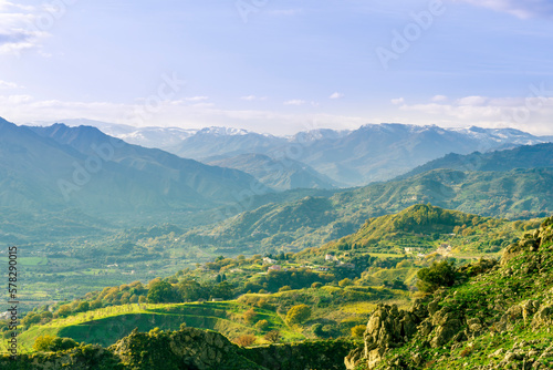 picturesque view in a green mountain valley among slopes and hills with sunny plantations on a rocky plato and nice cloudy sunset on background © Yaroslav