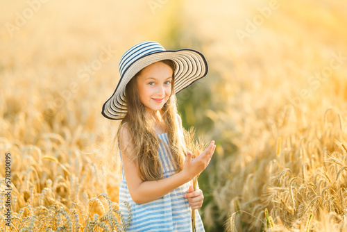 A pretty little girl stands in the middle of the field and holds a dry bunch of ripe golden rye. The child looks at the camera and smiles. photo