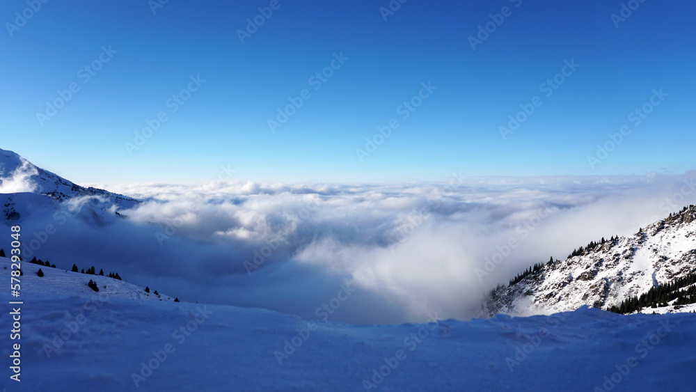 An epic ocean of clouds and fog in the winter mountains. Shots of huge powerful white clouds and clear sky in the mountains. There is snow, coniferous trees grow on slopes. Clouds come in waves