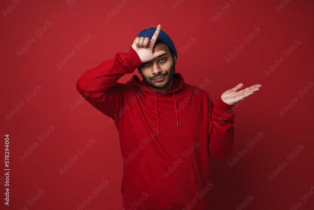 Indian man doing loser gesture and holding copyspace on palm isolated over red background Indian man doing loser gesture and holding copyspace on palm isolated over red background