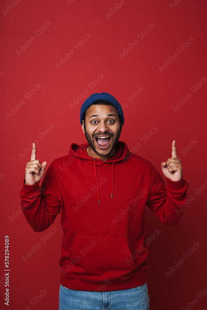 Young indian guy screaming and pointing fingers up at copy space isolated over red wall Young indian guy screaming and pointing fingers up at copy space isolated over red wall