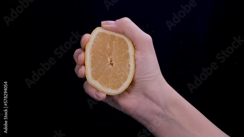 Woman squeezing a lemon half on black background. Citrus fruit source of vitamins and health concept. Slow motion
