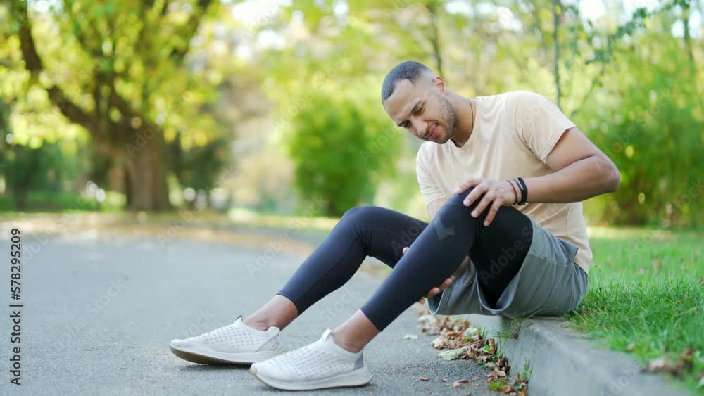 Young athlete runner sitting with muscle pain in city park. Man