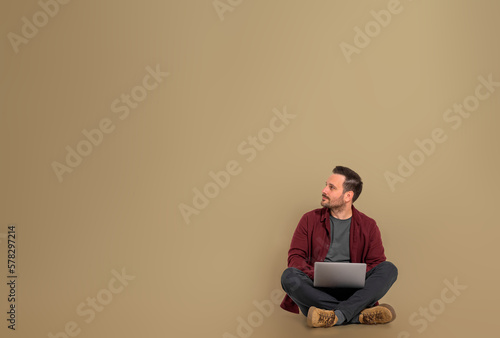 Foto Man using laptop looking away while sitting on beige brown background